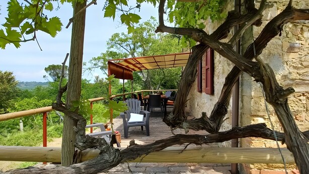Un área de estar al aire libre de estilo rústico con una pérgola, muros de piedra y vistas al campo.