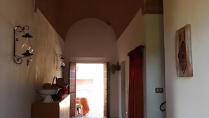 Un pasillo con techo de ladrillo, pared blanca con lámpara y puerta que da a otra habitación.