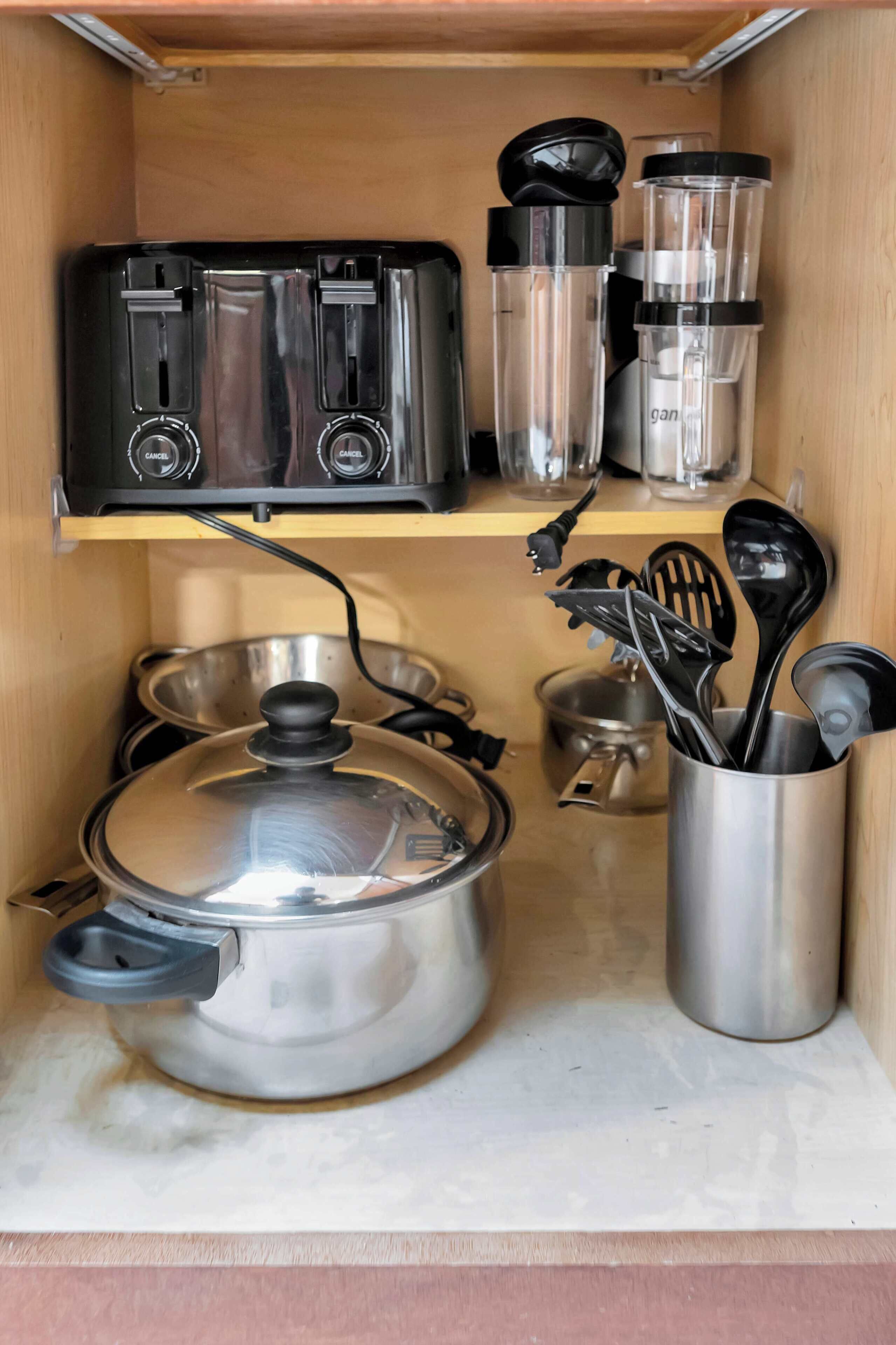 A compact kitchen with a stove, a pot, a toaster, and a utensil holder.