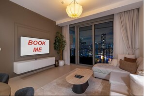 Ein modernes Wohnzimmer mit einem großen Fernsehbildschirm, der "BOOK ME" anzeigt, einer Couch, einem Couchtisch und Blick auf die Stadt durch große Fenster.