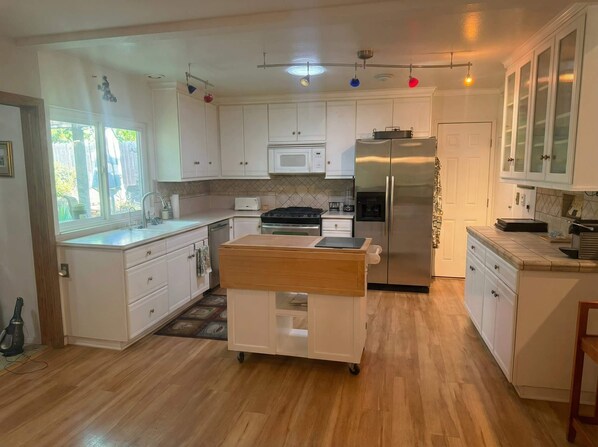 A modern kitchen with white cabinets, a stainless steel refrigerator, a microwave, and a gas stove. - Mid-century Ojai Escape Hot Tub Serene Garden (Ojai)