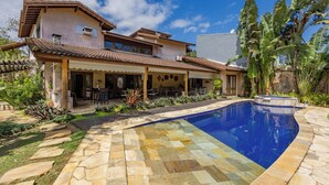 Una casa con piscina, mobiliario exterior y plantas tropicales.