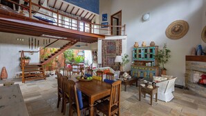 Amplia sala de estar con escalera de madera, una mesa de comedor con sillas, un sofá y un mueble con adornos.