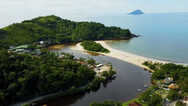 Vista aérea de una zona costera con playa, una pequeña isla con edificios y una gran masa de agua.