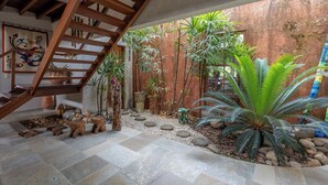 Una escalera conduce a un balcón con vistas a un jardín con diversas plantas y un muro rústico.