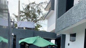 Une terrasse extérieure moderne, avec une table et des chaises sous un parasol vert, un extincteur et une petite plante sur le côté.