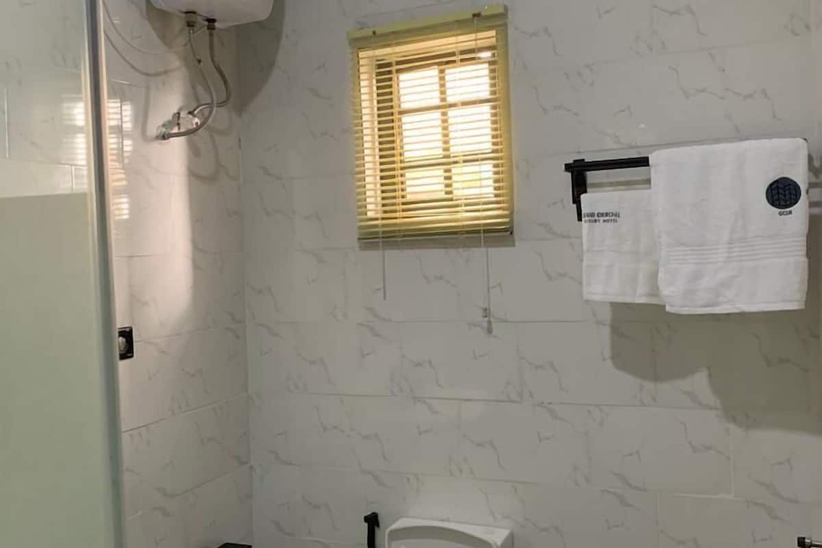 Ein Badezimmer mit Toilette, einem Handtrockner, einem Fenster mit Jalousien und einem Handtuchhalter mit Handtüchern.