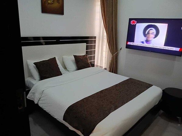 A hotel room with a bed, a television mounted on the wall, and a window with curtains. - Grand Churchill Luxury Hotel (Lagos)