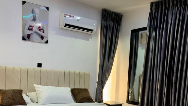 Une chambre d’hôtel moderne dotée d’un grand lit, d’un téléviseur à écran plat, d’un luminaire au plafond et d’une fenêtre avec des rideaux.
