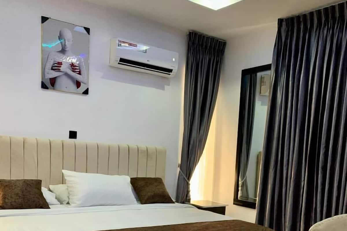 Ein modernes Hotelzimmer mit einem großen Bett, einem Flachbildfernseher, einer Deckenleuchte und einem Fenster mit Vorhängen.