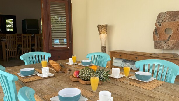 A breakfast table set with plates, cups, a loaf of bread, a pineapple, and a bottle of orange juice. - Bright 3-Bedroom Villa Near Eagle & Palm Beach (Noord)