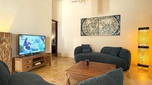 A living room with a TV, sofas, a coffee table, and a decorative wall piece. - Bright 3-Bedroom Villa Near Eagle & Palm Beach (Noord)