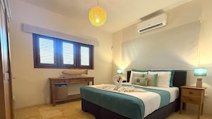 A bedroom with a bed, bedside tables, a desk, a fish decoration, and a window with blinds. - Bright 3-Bedroom Villa Near Eagle & Palm Beach (Noord)