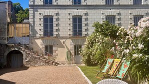 A large stone building with multiple windows and a well-maintained lawn. There are wicker chairs with floral cushions and a small garden area with flowers. - Maison Adrienne / Chambre beige Charming guest house, 4 km from Beauval Zoo (Saint-Aignan)