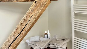 A bathroom with a wooden beam ceiling, a white towel rack, and a wooden table with towels and toiletries. - Maison Adrienne / Chambre beige Charming guest house, 4 km from Beauval Zoo (Saint-Aignan)