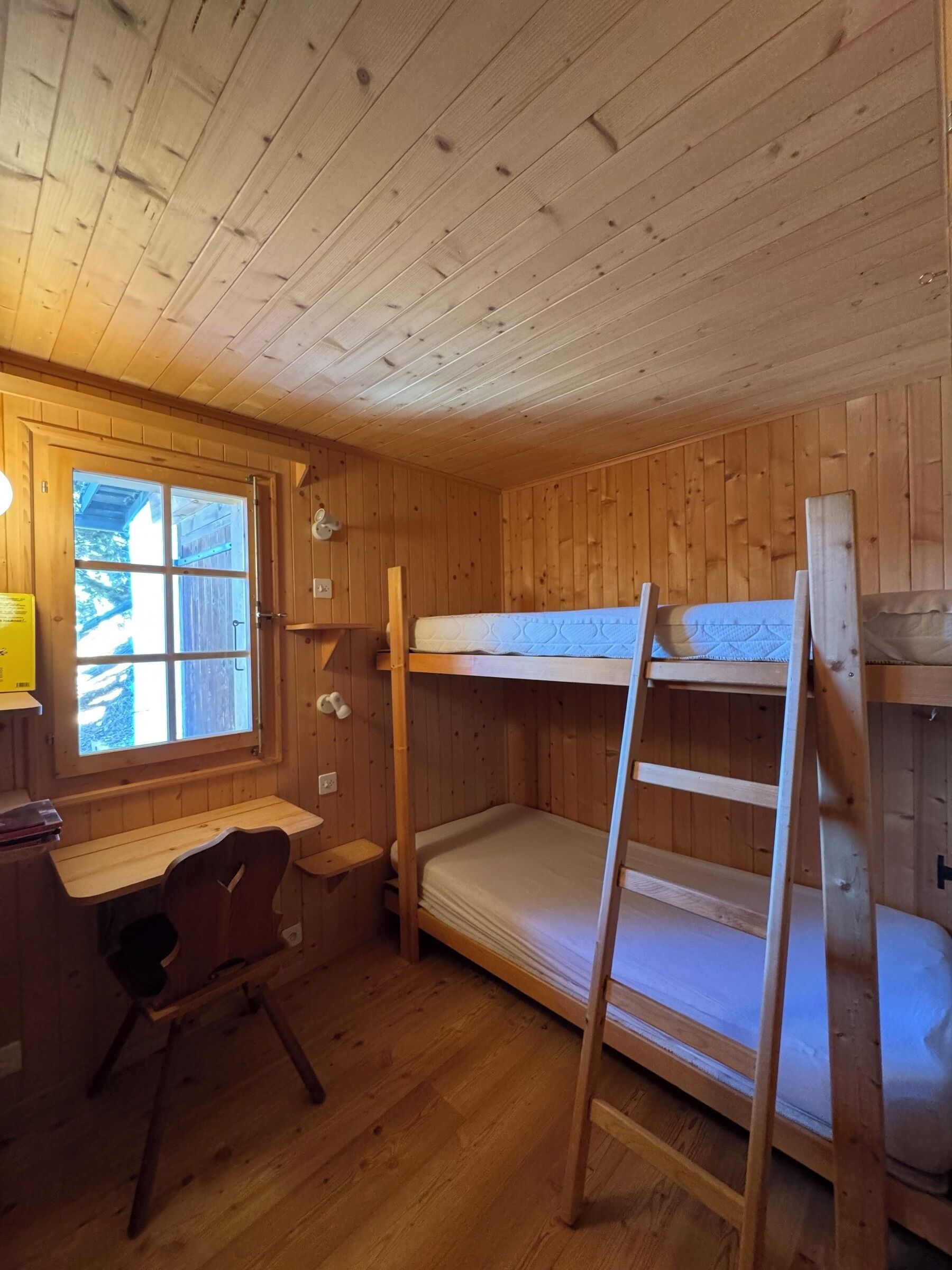 Una habitación tipo cabaña de madera con literas, un escritorio y una ventana.