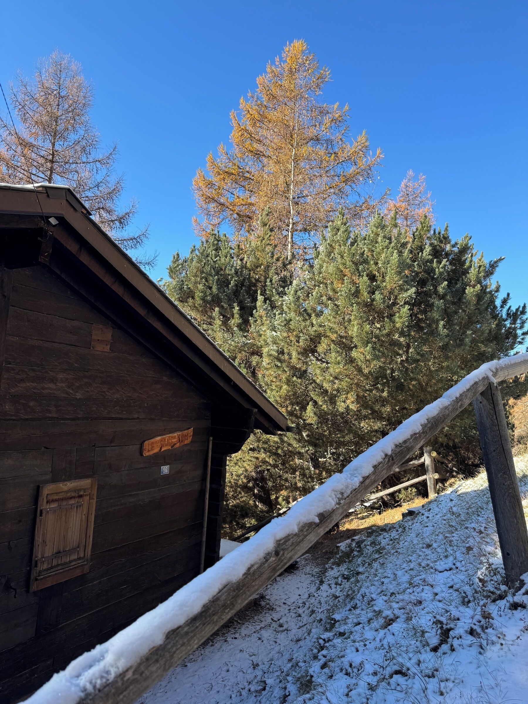 Een houten hutje met een sneeuwbedekte dak en een houten omheining.