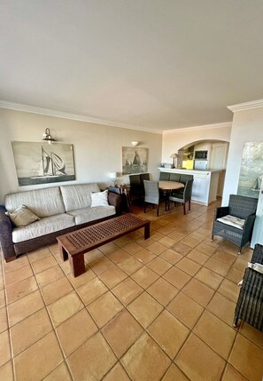 A living room with a sofa, a coffee table, and a dining area with chairs and a table. - Sea view apartment, 6/8 people. Vacation Village (Grimaud)