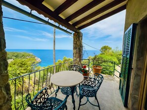 Un balcon avec une table ronde et des chaises, une vue sur la mer et un mur en pierre.