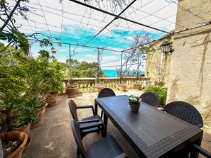 Une terrasse extérieure avec une table et des chaises, des plantes en pot et une vue sur la mer.