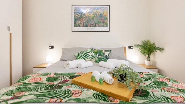 Een net opgemaakt bed met opgerolde handdoeken, een dienblad met toiletartikelen, en een ingelijst schilderwerk van Claude Monet erboven.