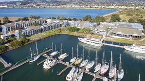 Una marina con diverse imbarcazioni ormeggiate, un'imponente yacht bianca e un complesso di edifici con tetto piano.