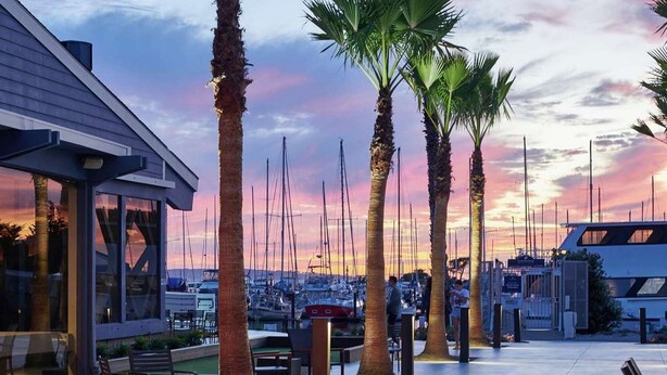 Patio sul lungomare con palme, posti a sedere all'aperto e uno sfondo che mostra un porto turistico.