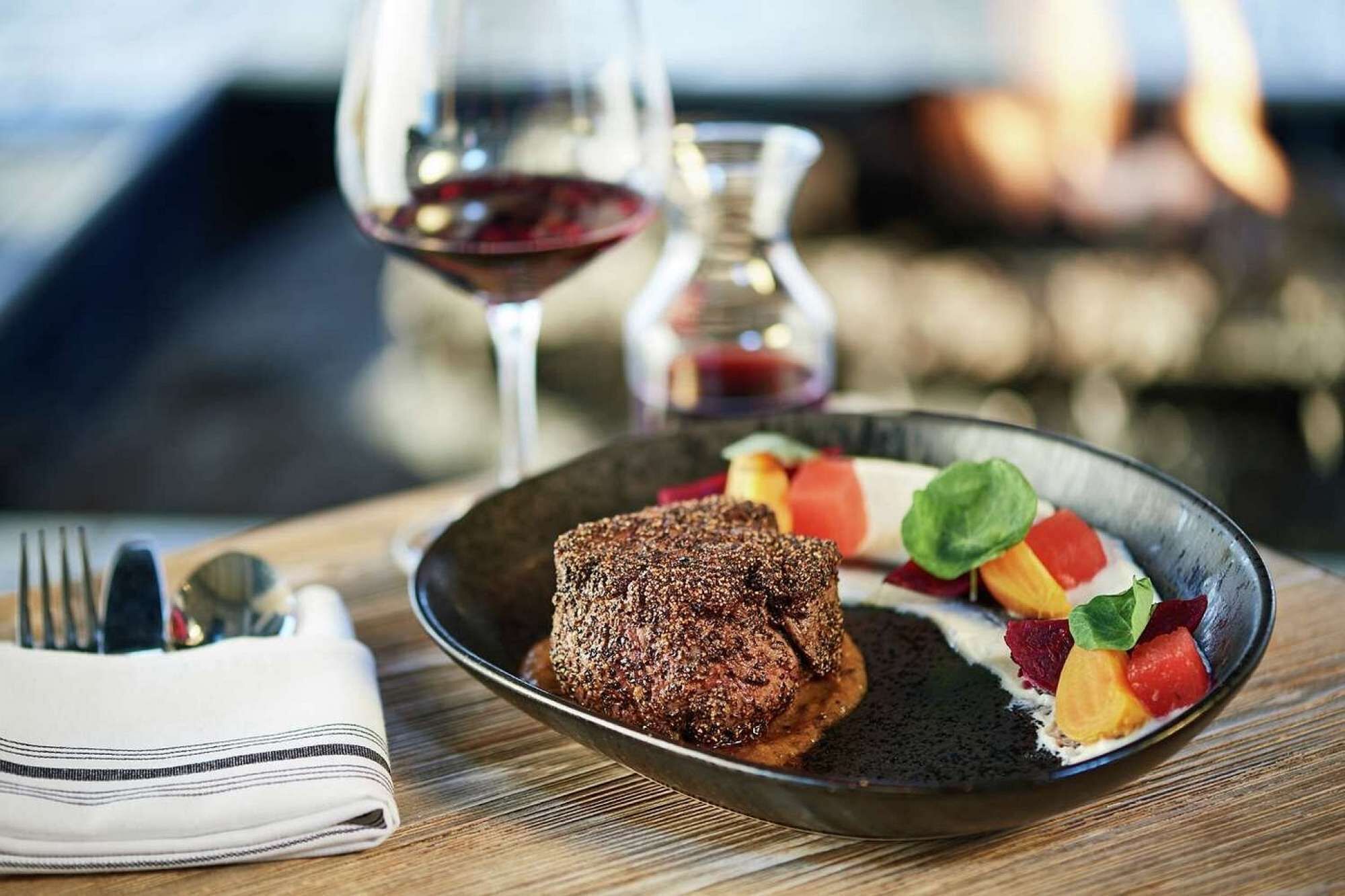 A plate with a meat dish and colorful fruit on a wooden table.