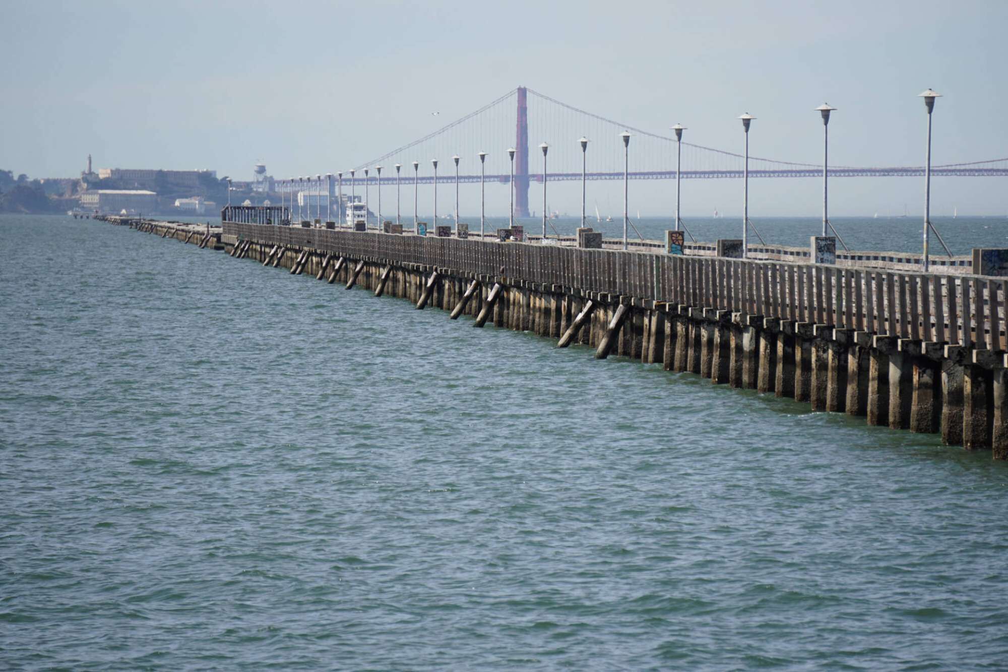Un muelle largo que se adentra en el agua, con un puente al fondo.