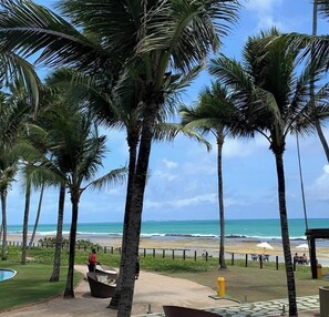 Une vue sur la plage, avec des palmiers, une piscine et une zone de plage agrémentée de parasols.