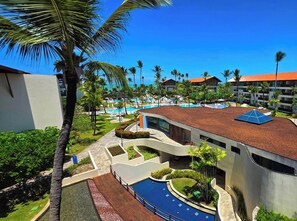 Ein Resort mit Schwimmbad, Palmen und einem modernen Gebäude mit gewölbter Dachlinie.