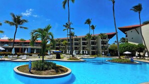 Un área de piscina de hotel con varias piscinas, sillas de descanso y palmeras.