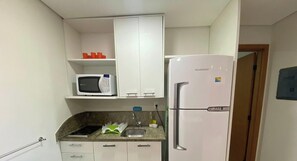 Eine kleine Küche mit weißen Schränken, einer Mikrowelle, einem Kühlschrank und einem Spülbecken.