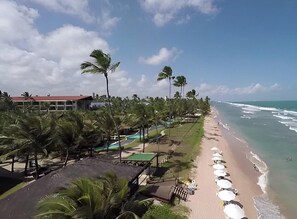 Ett semesterparadis vid stranden med palmer, en pool och en strand med parasoller.