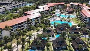 Un resort con varias edificaciones, una piscina central y palmeras aledañas.