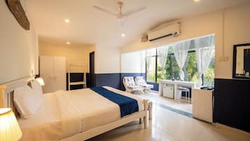 A hotel room with a bed, a desk, a chair, a wardrobe, and a window with a view of greenery.