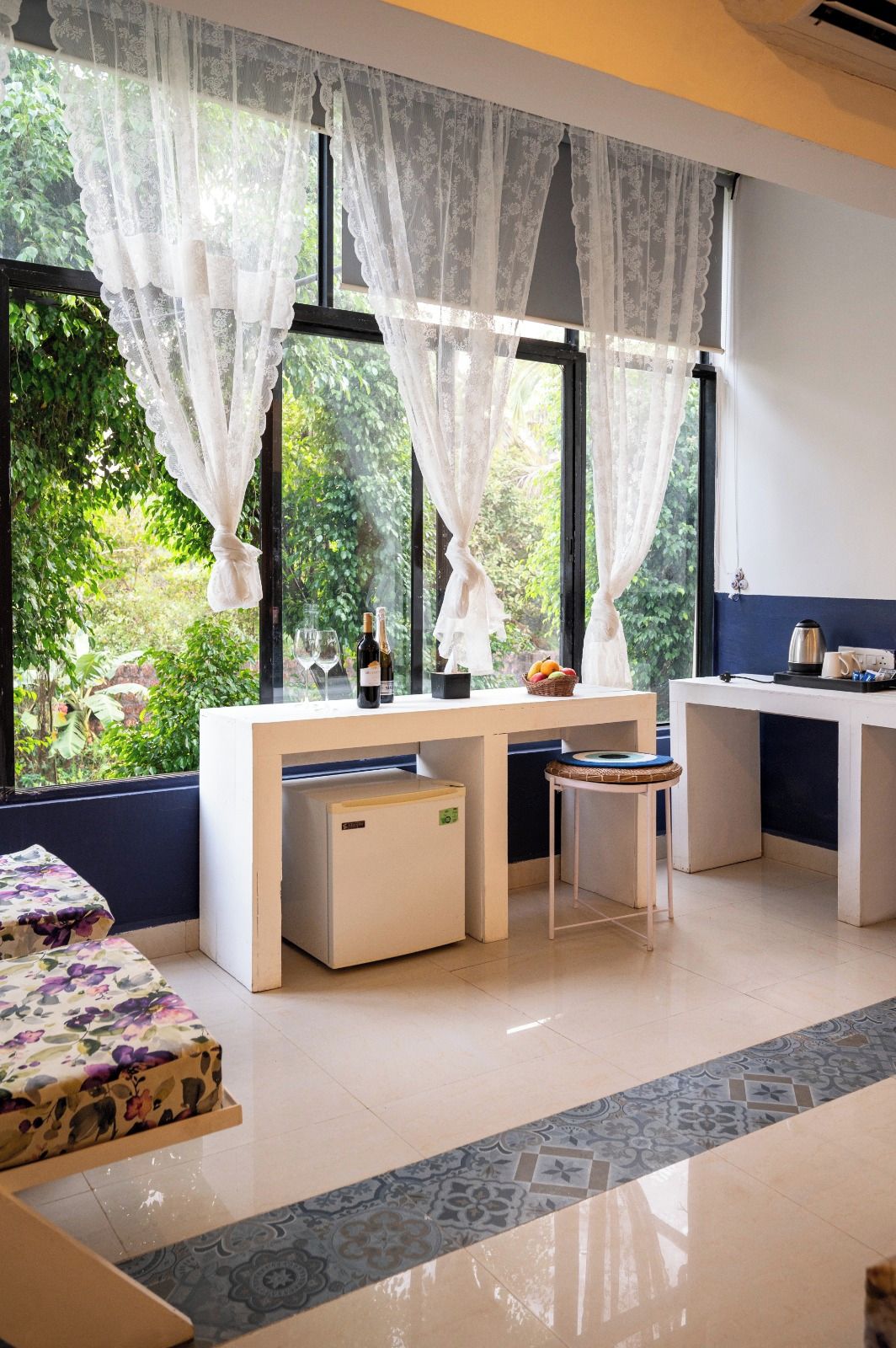 Una habitación con escritorio, silla, mesita y sofá. Hay ventanas con cortinas, vistas a zonas verdes y suelo de baldosas.