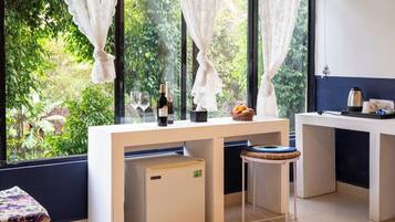 Una habitación con escritorio, silla, mesita y sofá. Hay ventanas con cortinas, vistas a zonas verdes y suelo de baldosas.