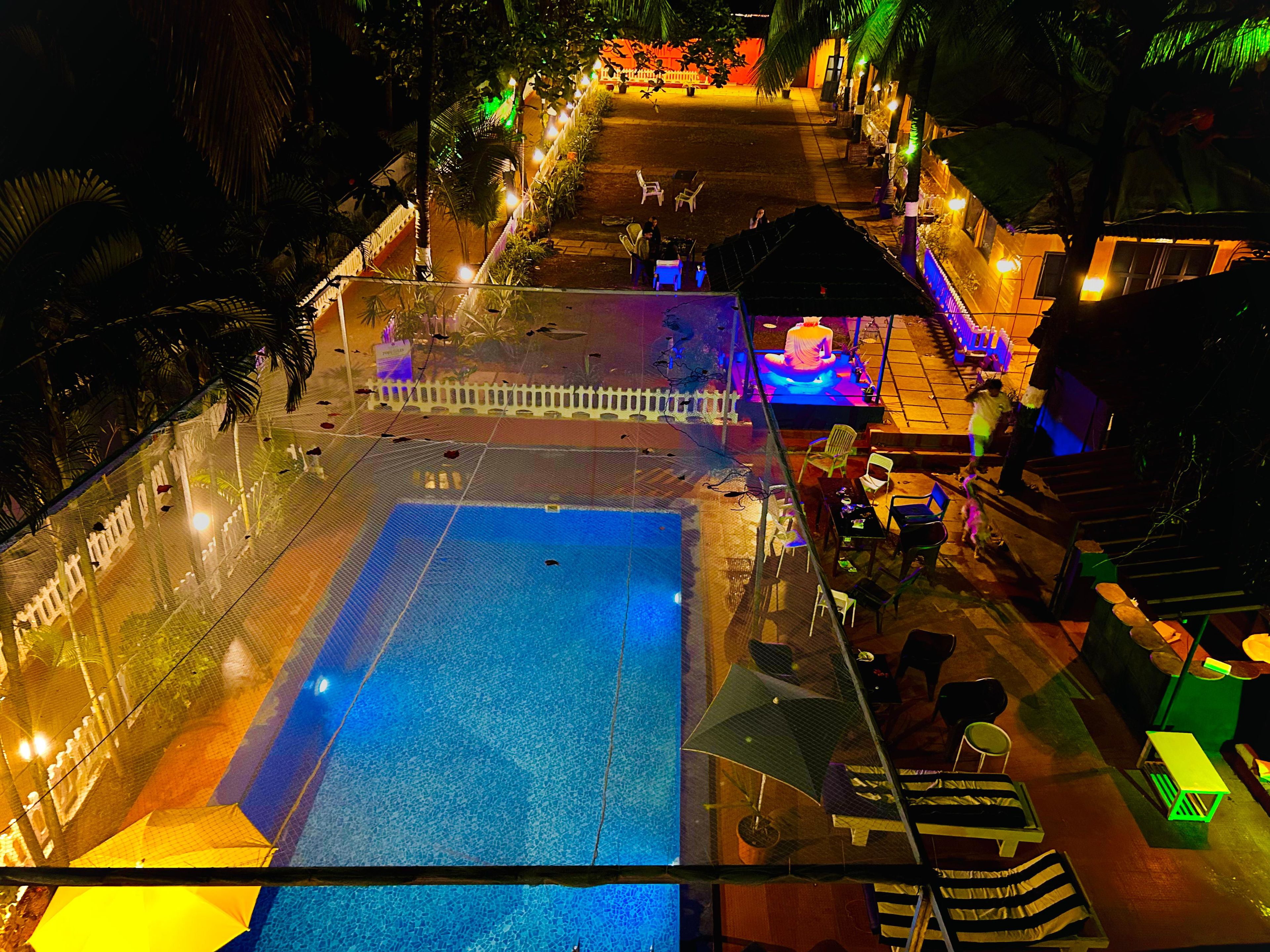 Piscina externa com área cercada, cadeiras de descanso e um pequeno palco.