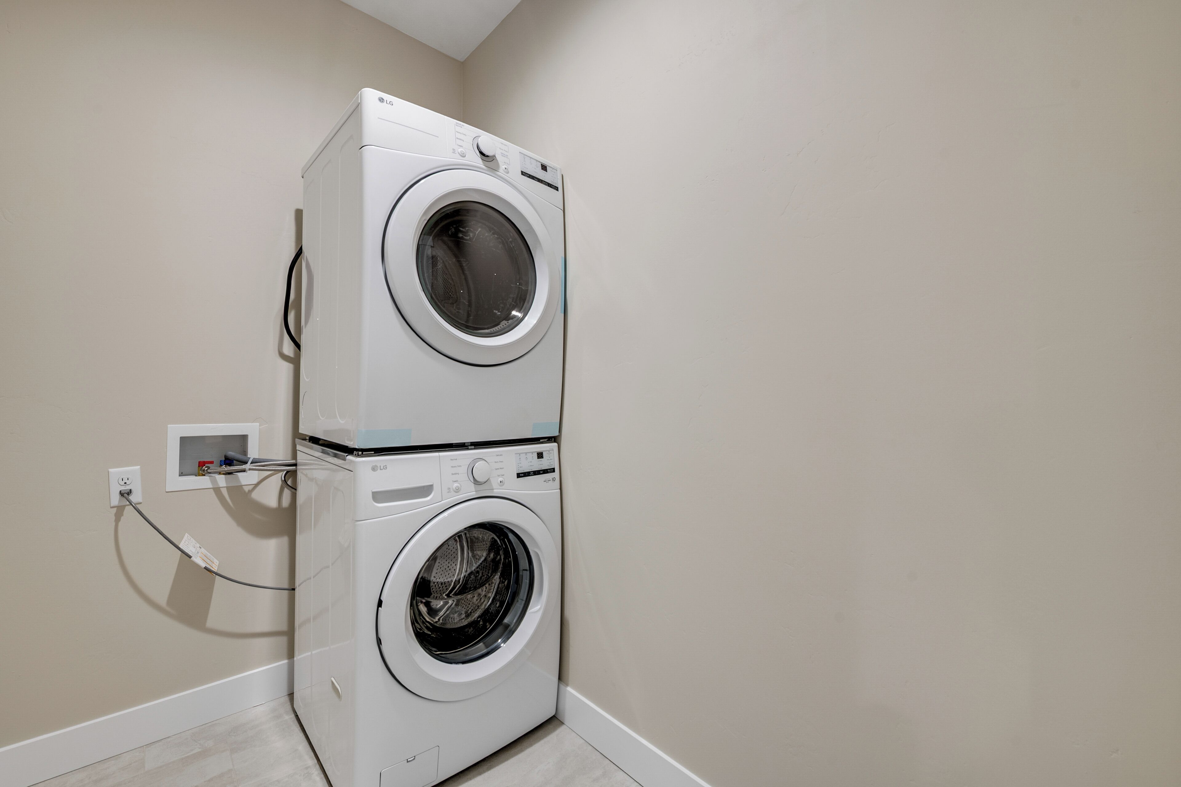 A stacked washer and dryer unit in a corner with a power outlet on the wall.