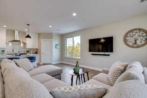 A modern living room with a large sectional sofa, a small round table, and a TV mounted on the wall. - Ski Resorts & SLC Fun! Brand New Millcreek Home (Salt Lake City)
