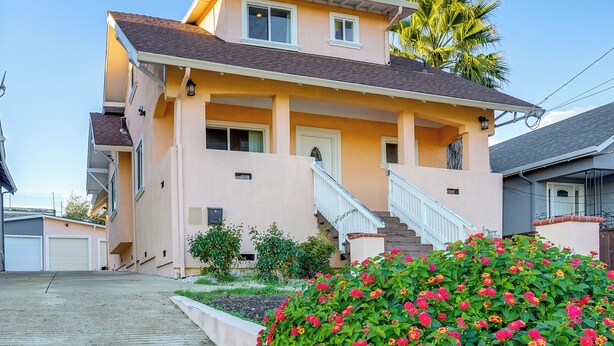 Ein zweistöckiges Haus mit Veranda, Treppe und einem gepflegten Garten mit roten Blumen.