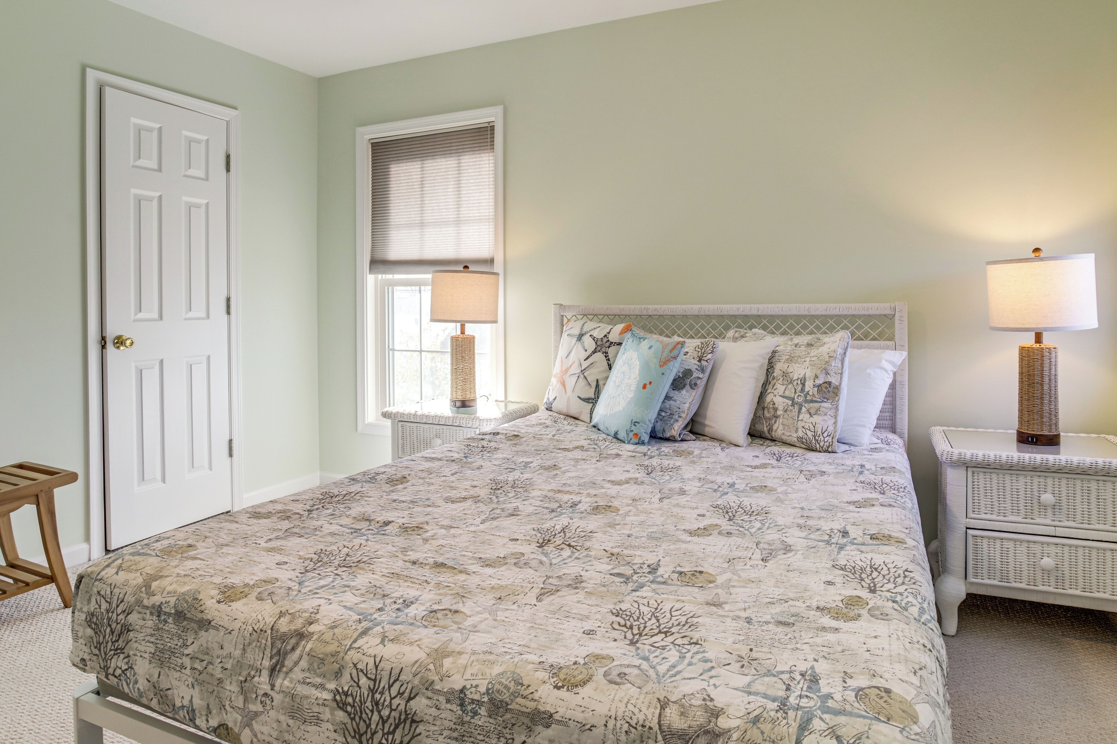 A bedroom with a large bed, two bedside tables with lamps, a window with blinds, and a door.