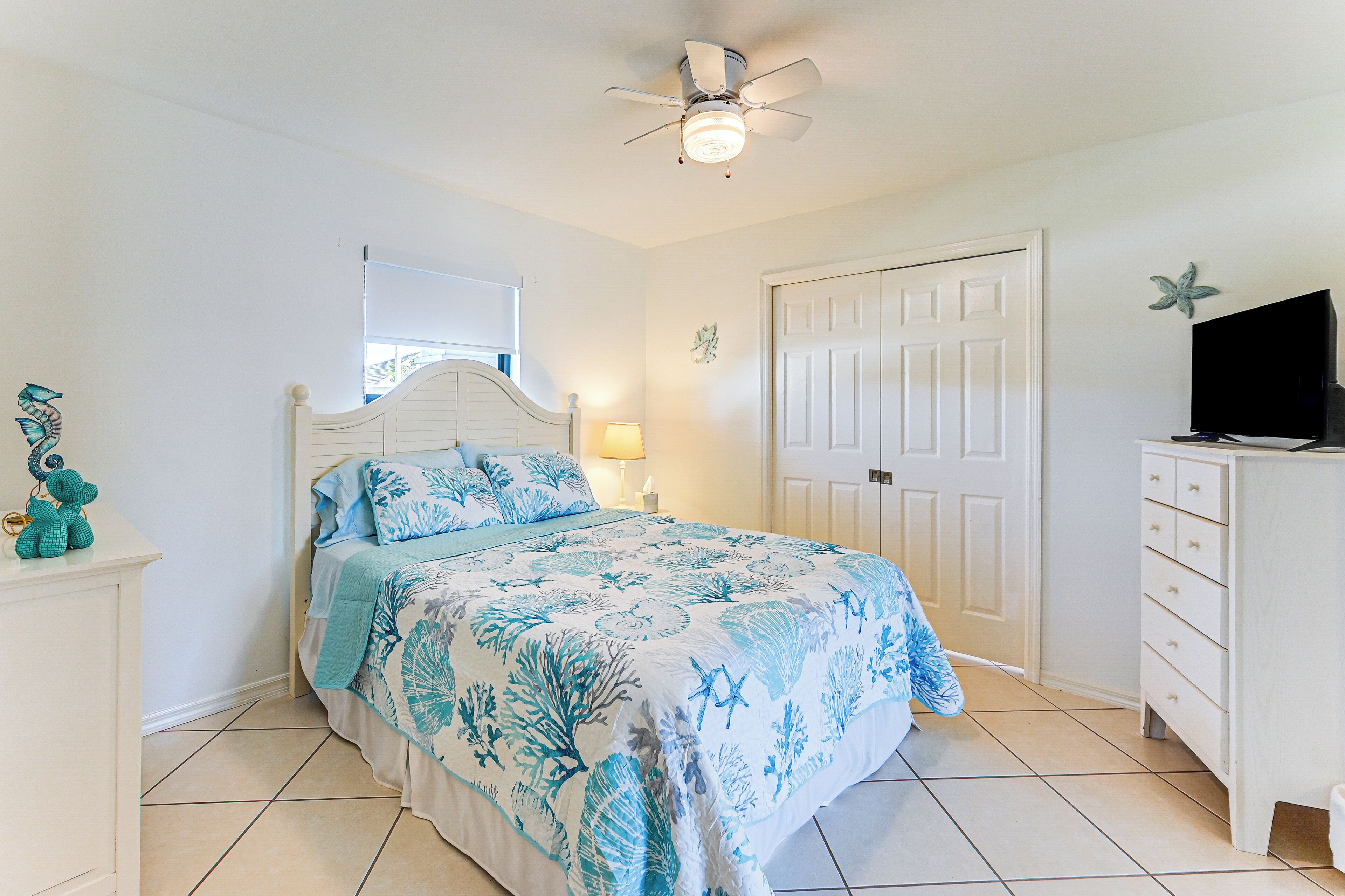A bedroom with a bed, a nightstand, a dresser, a television, and a ceiling fan.