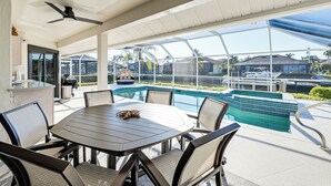 A covered outdoor area with a pool, a dining table with chairs, and a bar area. - Canal-front Luxury Pool, Boat & Relax in Marco (Marco Island)