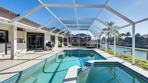 A swimming pool with a covered patio area, a view of the water, and a building with a tiled roof. - Canal-front Luxury Pool, Boat & Relax in Marco (Marco Island)