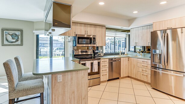 A modern kitchen with stainless steel appliances, wooden cabinets, and a large island with seating. - Canal-front Luxury Pool, Boat & Relax in Marco (Marco Island)