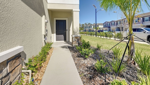 A residential street with a sidewalk leading to a house with a dark front door and a stone base.