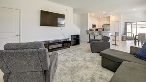 A modern living room with a flat-screen TV, grey sofas, a fluffy rug, and a kitchen in the background.