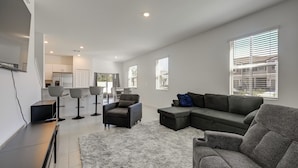 A modern living room with a sectional sofa, a coffee table, and a TV on a stand. There are four chairs and a rug on the floor.
